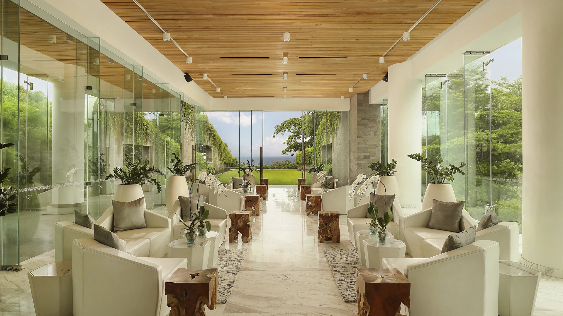 Bright pavilion lounge with rows of armchairs, an orchid and an ocean view beyond the lawn